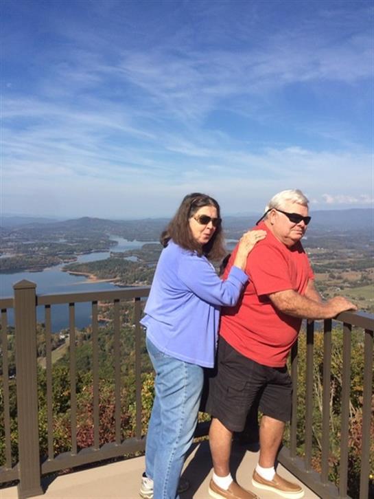 A couple stands by a railing, taking in the expansive view of the river and valley below.