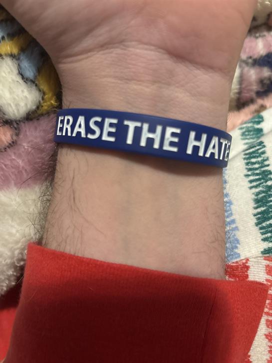 A blue wristband reads Erase the Hate against a vivid, patterned blanket.