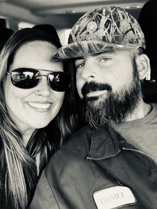 A happy couple poses for a selfie, both wearing sunglasses and smiling widely in a vehicle.
