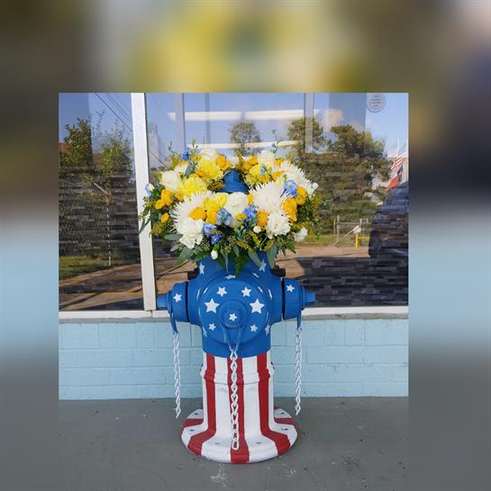 A vibrant fire hydrant, painted with red, white, and blue, holds a bouquet of flowers in a city.
