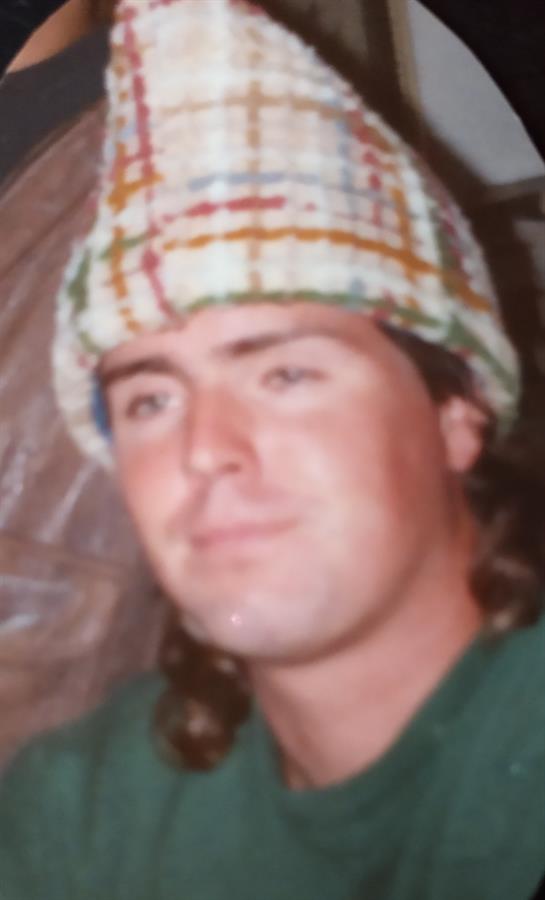Young man smiles while wearing a multicolored knit hat in an indoor, cozy environment.