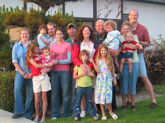 A large family enjoys a gathering outdoors, smiling and posing together in a park setting.