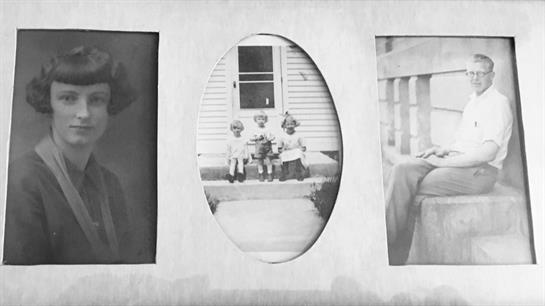 Three children in vintage clothes smile on a porch in a cozy family setting.