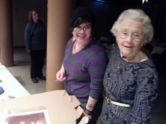Two women smile and interact happily, showcasing a warm moment during a social gathering.