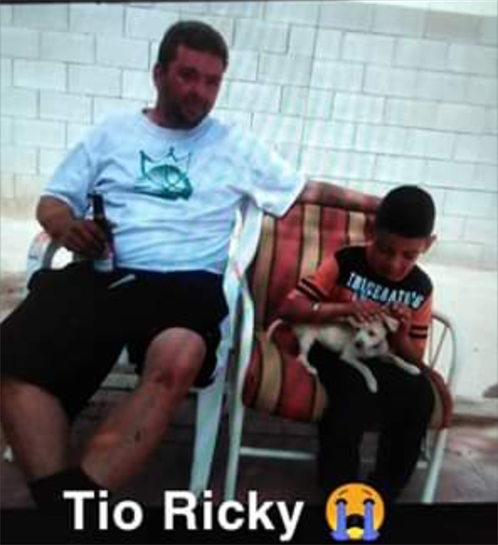 Uncle relaxes on a chair with a drink while a child plays with a puppy on a sunny day.