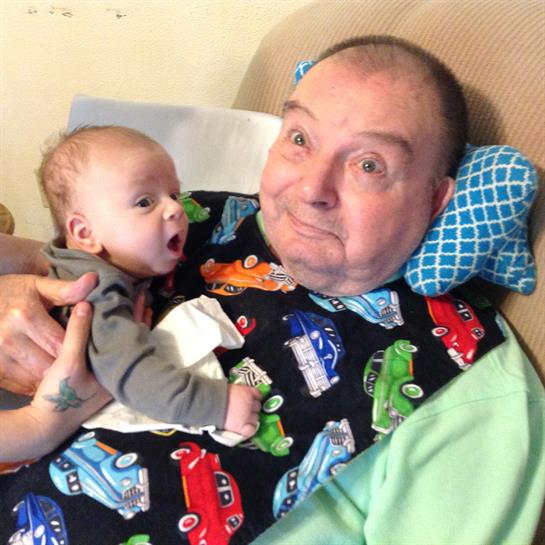 Elderly man smiles at baby in his arms, creating a heartwarming family moment indoors.