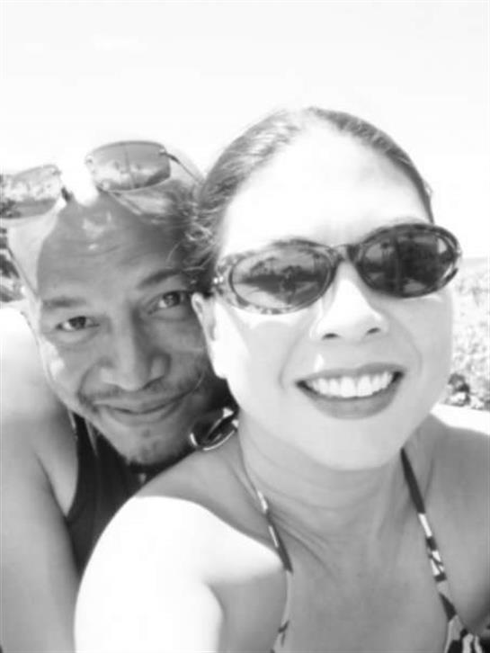 Two people pose for a selfie at the beach, smiling under the bright sun with sunglasses on.