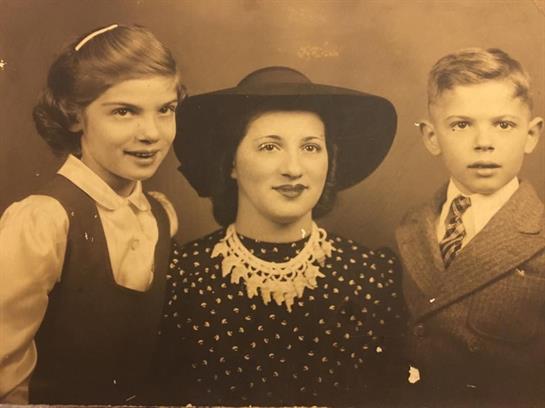 Two children stand beside a woman wearing a hat, displaying affection and family bonds.