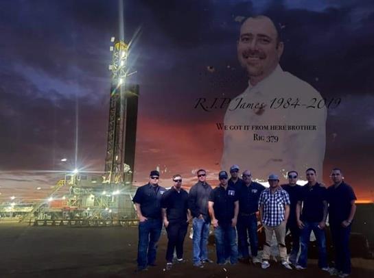 Group of workers gathers for a picture at a wellsite with a memorial backdrop during sunset.