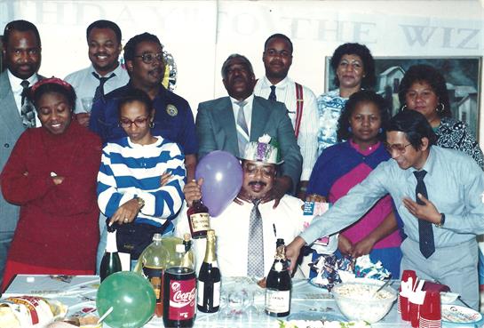Group of friends and family enjoy a festive gathering with drinks, party hats, and balloons.