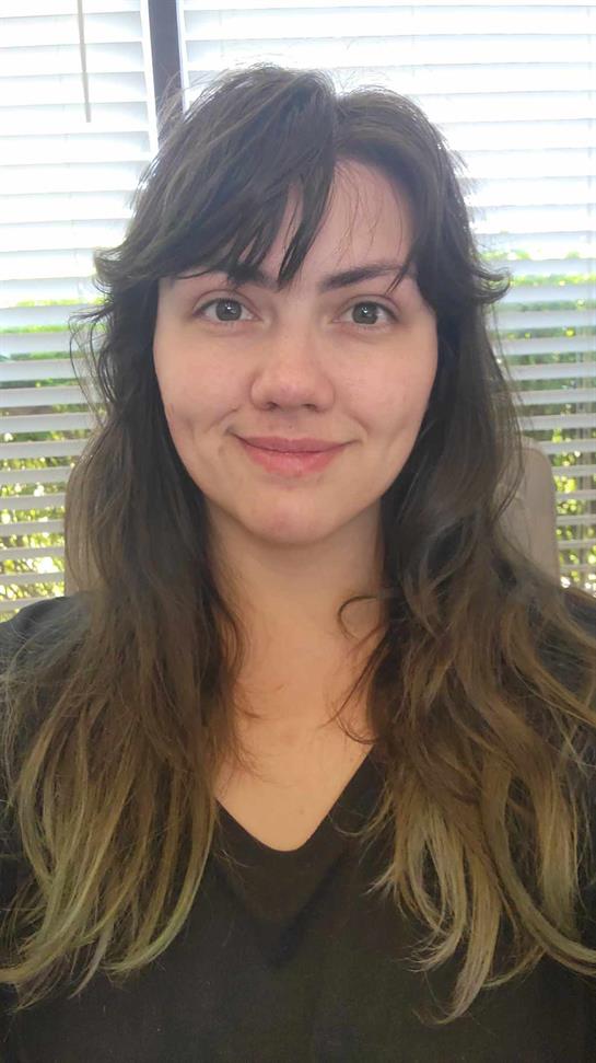A young woman with long hair displays a friendly smile while sitting indoors.