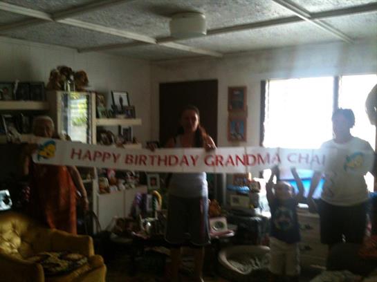 Relatives celebrate grandma's birthday joyfully with a banner in the living room.