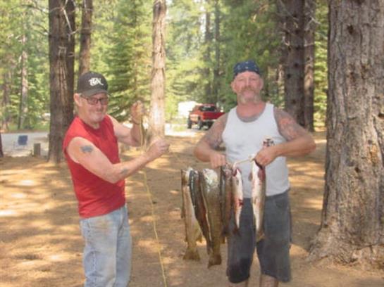 Two friends stand in a forest showing off their freshly caught fish after a successful outing.