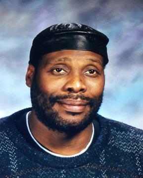 A man with facial hair smiles gently in a cap and cozy sweater, creating warmth.