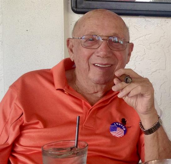Elderly gentleman enjoys a drink at a table, smiling and engaging in conversation with friends.