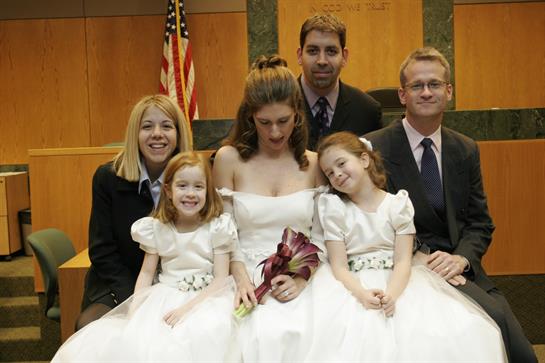 A newlywed couple poses for a group photo with friends and family at a wedding ceremony venue.