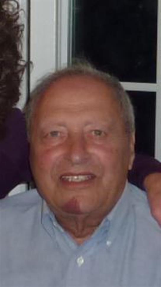 Older man smiles brightly while sitting comfortably among friends during a casual gathering at home.