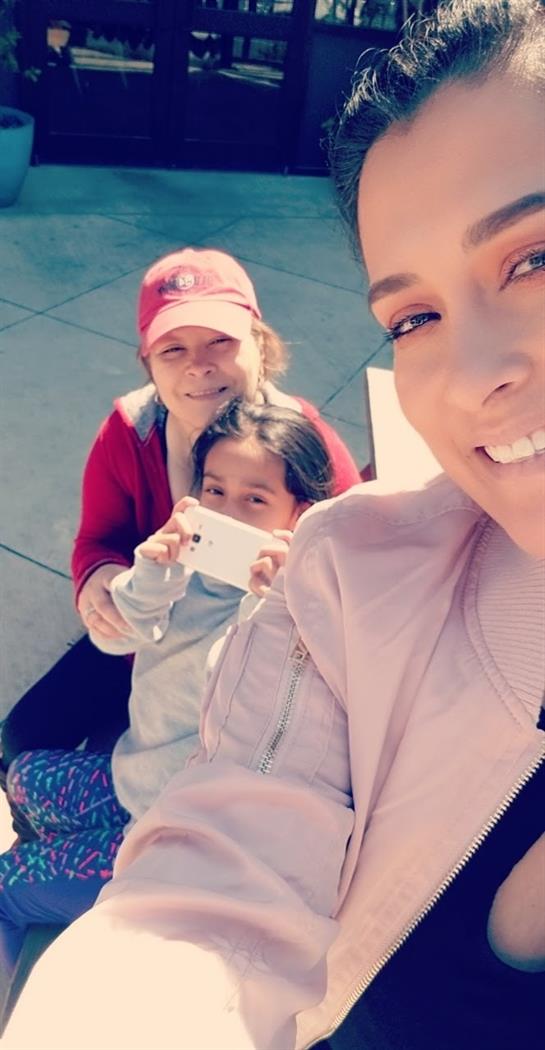 Three individuals share a joyful moment outside, basking in the sun and taking photos.