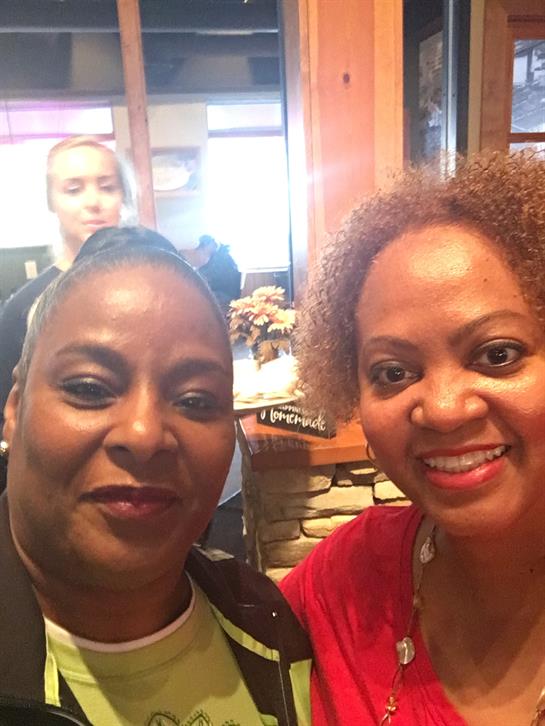 Two friends smile brightly while taking a selfie at a cafe, capturing their joyful moment together.