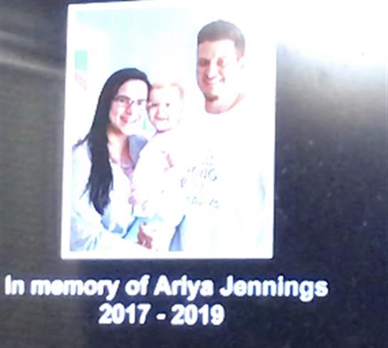 Tribute display with Arya Jennings' family portrait, surrounded by loved ones, full of emotion.