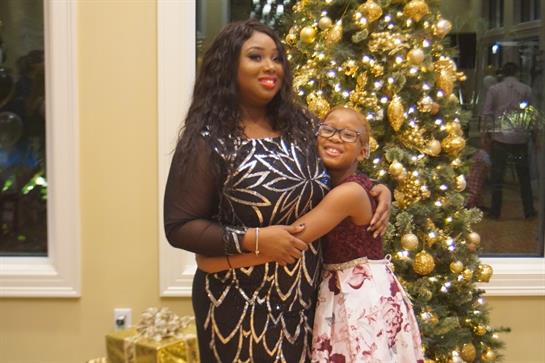 Mother and daughter share a joyful embrace in front of a beautifully decorated holiday tree.