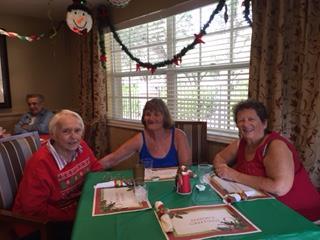 Three friends sit together at a table decorated for the holidays, sharing laughter and good company.