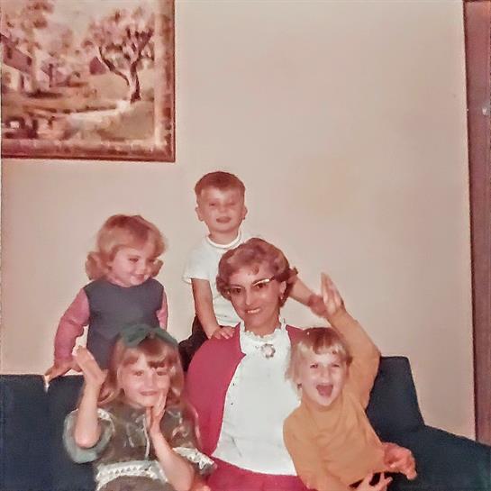 Joyful children interact with an adult on a couch in a cozy living room setting.