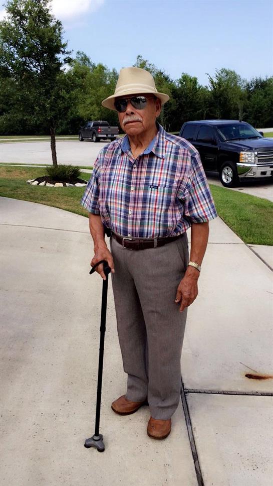 An elderly man is on his residential driveway, using a cane and enjoying the sunny weather.