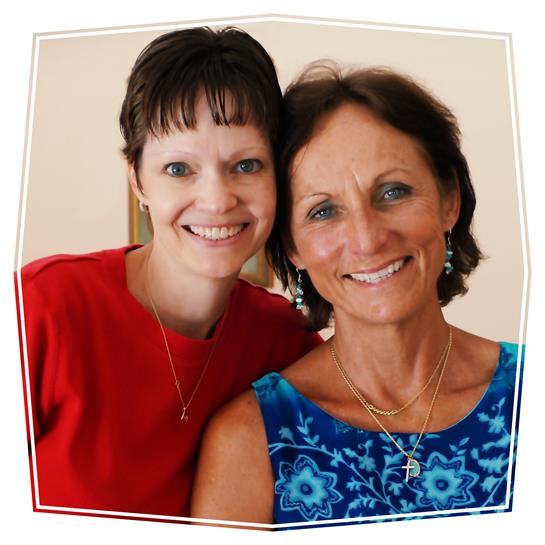 Two women share smiles in a bright indoor location, showcasing their friendship and happiness.