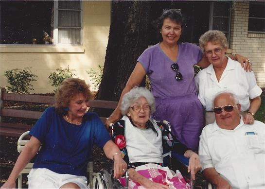 Family enjoys a warm summer day outdoors with a smiling elderly woman in a wheelchair.