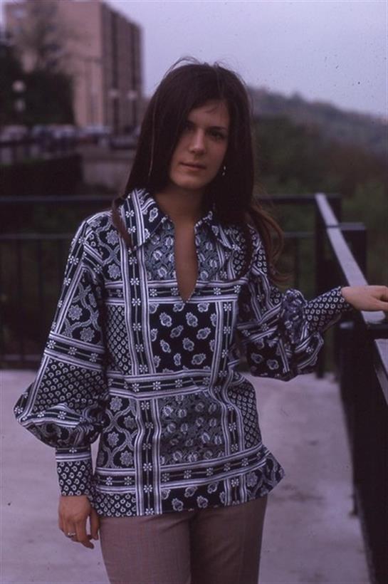 A model showcases a stylish patterned dress while standing on a balcony with a scenic view.