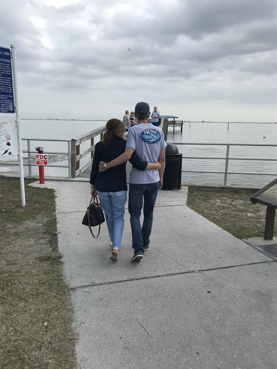 A couple walks closely together on the pier as waves gently lap against the shore.