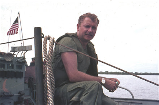 A man dressed in military attire sits on a boat, enjoying the serene view of the water.