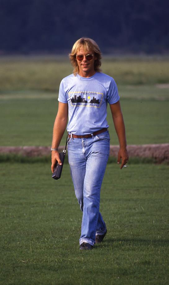 A person walks confidently across a grassy area wearing a casual outfit, enjoying the weather.