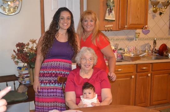 Joyful family moment in a kitchen as three women share laughter while holding an infant.