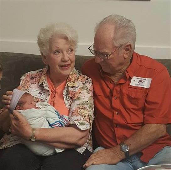 Elderly couple cherishes special moments with their newborn grandchild at a family gathering.