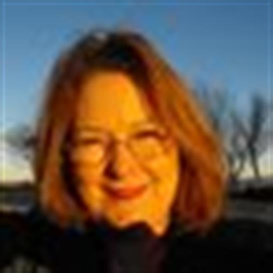 A woman with glasses enjoys the sunset, smiling at the camera amidst a natural landscape.