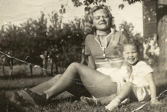 A joyful mother sits with her smiling daughter on the grass during a sunny day in the park.