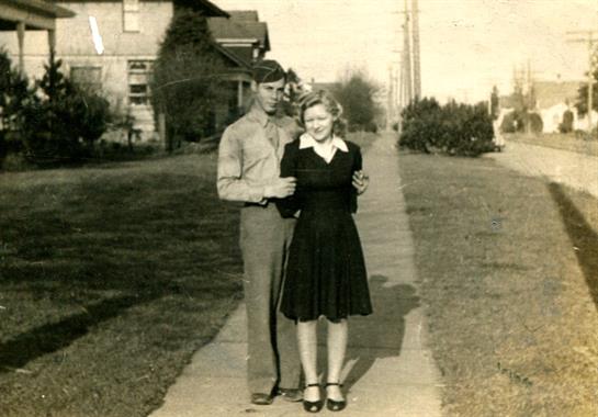 A happy couple in vintage clothes poses together on a sunny sidewalk.