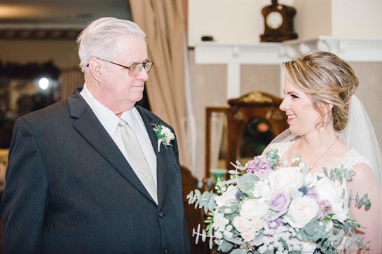 A father looks lovingly at his daughter, who is dressed in a beautiful wedding gown.