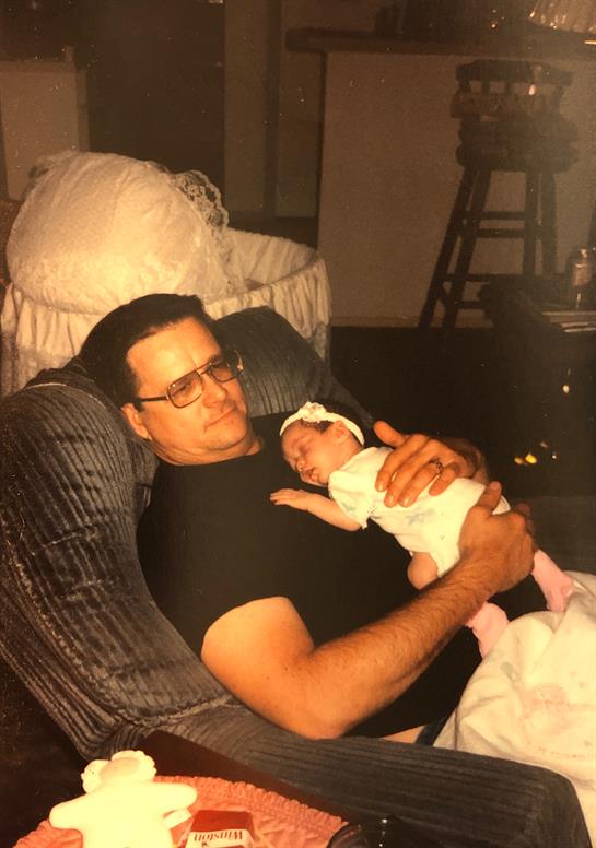 Man embraces his infant child while relaxing on a couch in a warm, inviting space.