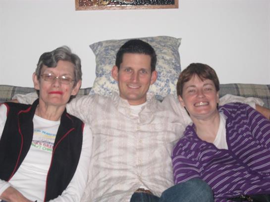 Three family members pose happily on a couch, enjoying a moment together in their home.