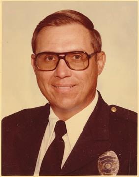 A smiling former police officer in uniform stands confidently, reflecting dedication.
