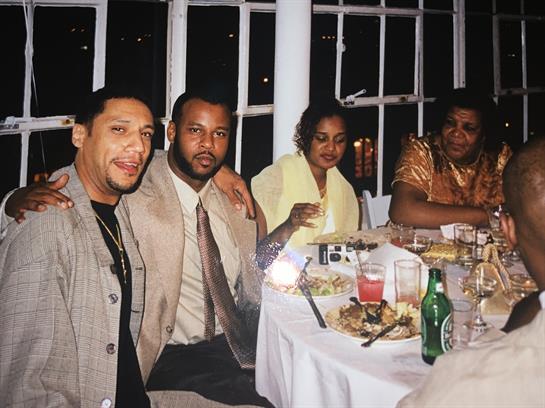 Four people enjoy food and drinks while chatting at a festive evening table.