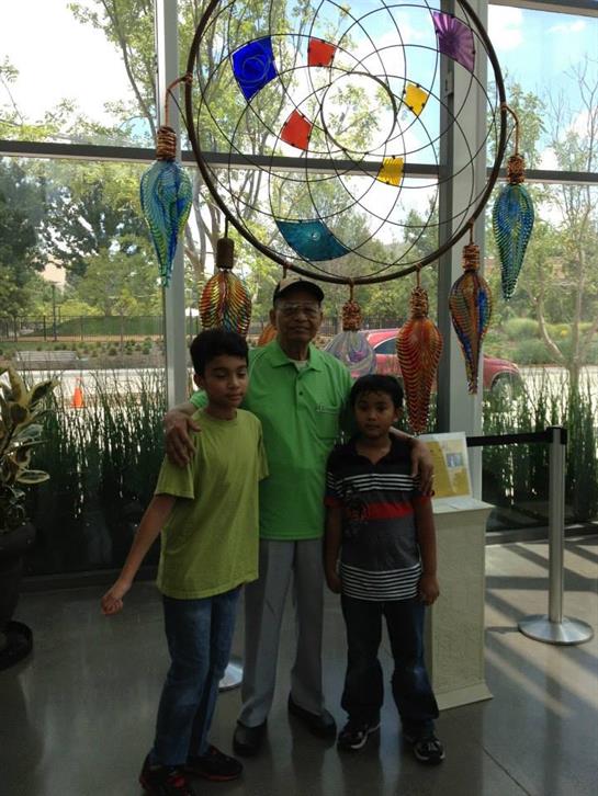 Two children pose with an adult in a botanical garden showcasing unique art pieces.
