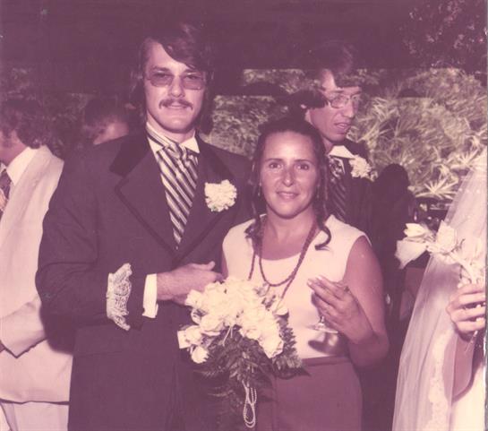 Happy couple in formal wear holding flowers, smiling with friends at a wedding.
