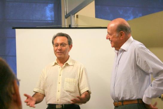 Two men are actively talking in an office environment while others listen attentively.