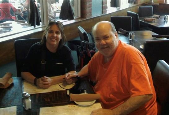 Two people are smiling together at a table in a cafe, sharing a friendly moment while dining.