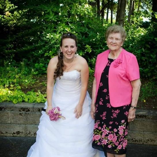 A happy bride poses with her grandmother amidst lush greenery, celebrating a special wedding day.