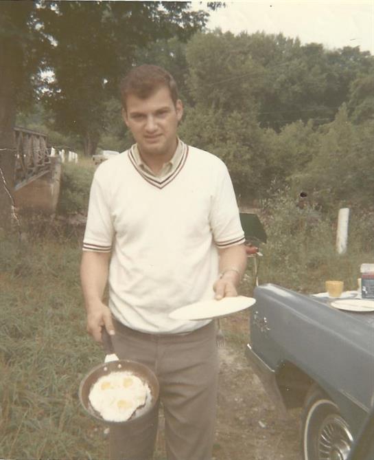 A man prepares food outside, showcasing his cooking skills with a frying pan and plate in hand.